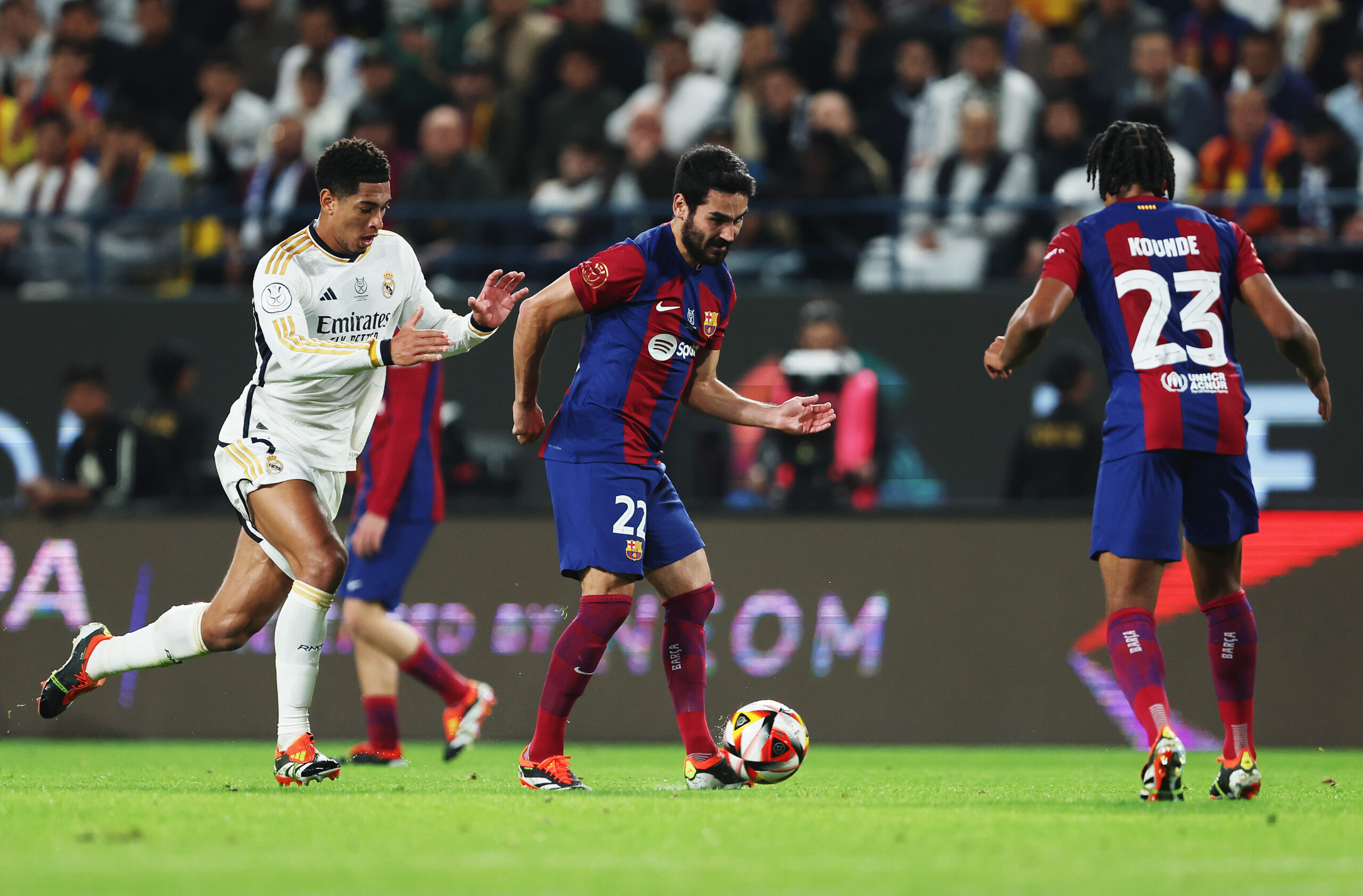 RIYADH, SAUDI ARABIA - JANUARY 14: Ilkay Gundogan of FC Barcelona passes the ball towards Jules Kounde of FC Barcelona under pressure from Jude Bellingham of Real Madrid during the Super Copa de España Final match between Real Madrid and FC Barcelona on January 14, 2024 in Riyadh, Saudi Arabia.