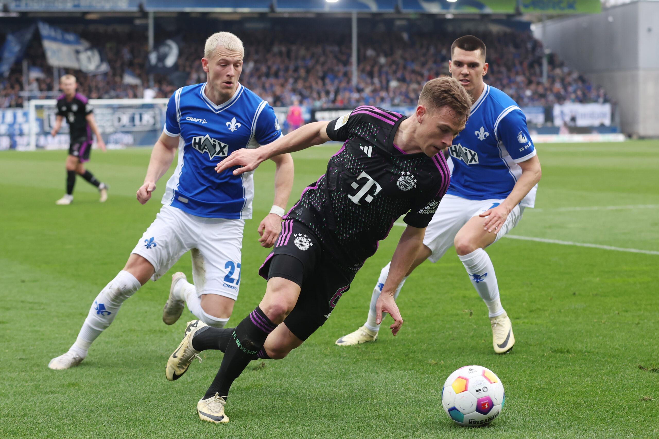 DARMSTADT, GERMANY - MARCH 16: Joshua Kimmich of Bayern Muenchen is challenged by Tim Skarke and Mathias Honsak of Darmstadt during the Bundesliga match between SV Darmstadt 98 and FC Bayern München at Merck-Stadion am Böllenfalltor on March 16, 2024 in Darmstadt, Germany.