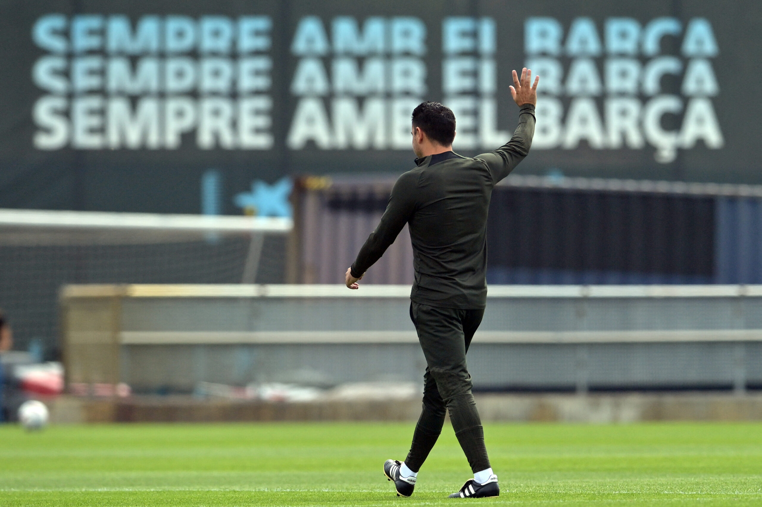 TOPSHOT - Barcelona Spanish coach Xavi waves during a training session at the Joan Gamper training ground in Sant Joan Despi, near Barcelona, on May 25, 2024. Text in the background reads in Catalan 