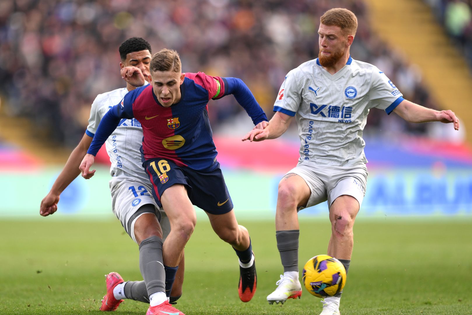 BARCELONA, SPAIN - FEBRUARY 02: Fermin Lopez of FC Barcelona is challenged by Santiago Mourino and Carlos Vicente of Deportivo Alaves during the LaLiga match between FC Barcelona and Deportivo Alaves at Estadi Olimpic Lluis Companys on February 02, 2025 in Barcelona, Spain.
