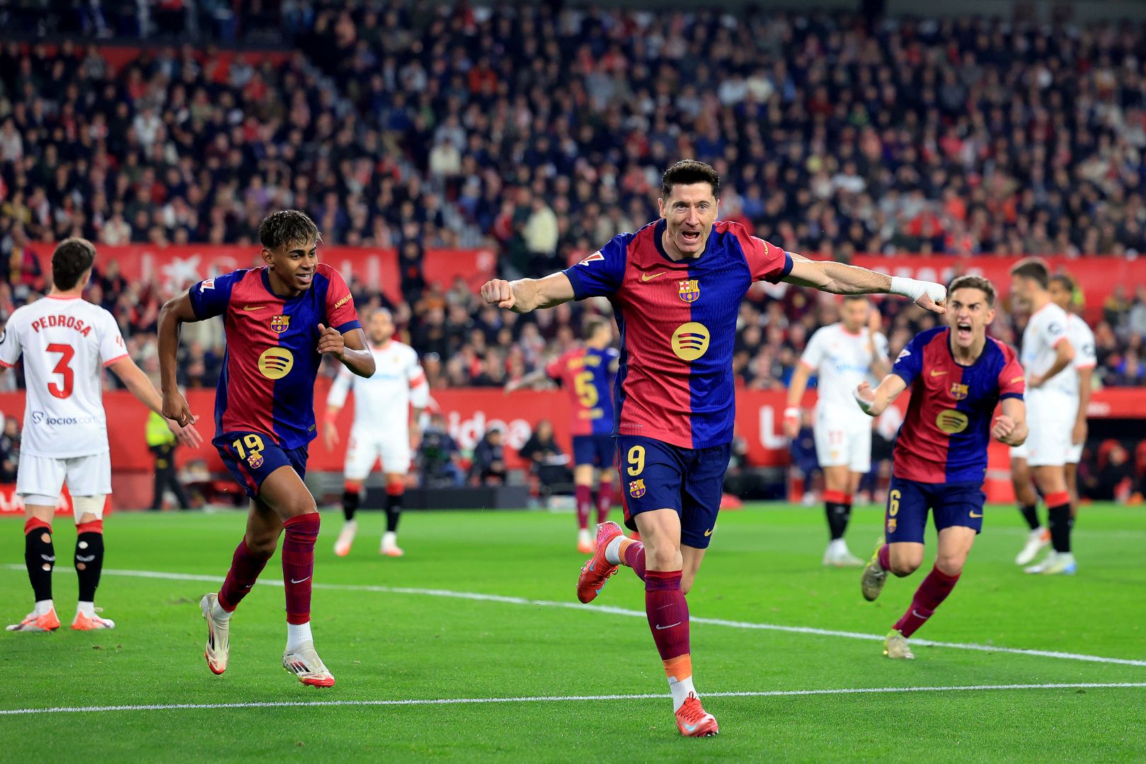 SEVILLE, SPAIN - FEBRUARY 09: Robert Lewandowski of FC Barcelona celebrates scoring his team's first goal with teammates Lamine Yamal and Gavi during the LaLiga match between Sevilla FC and FC Barcelona at Estadio Ramon Sanchez Pizjuan on February 09, 2025 in Seville, Spain.